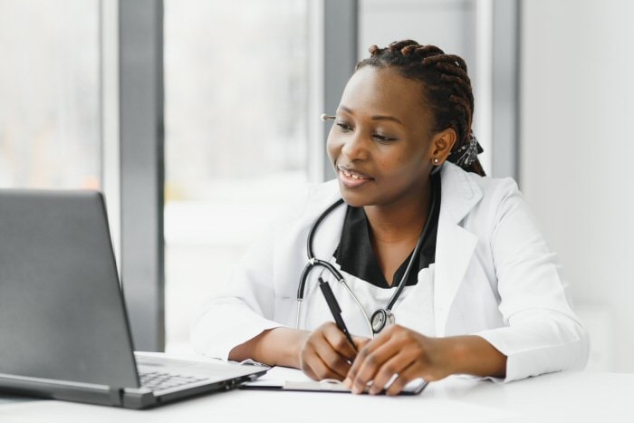 Physician taking notes while looking at a notebook computer